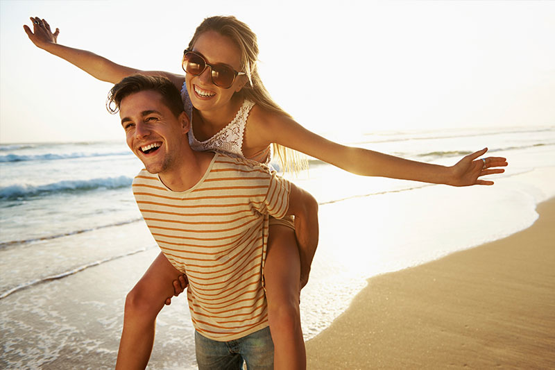 Man giving a women a piggy back ride on the beach on the cosmetic dentistry page