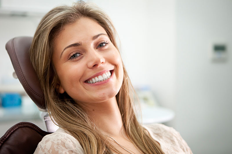 Woman smiling while sitting on dental chair on dental crowns page